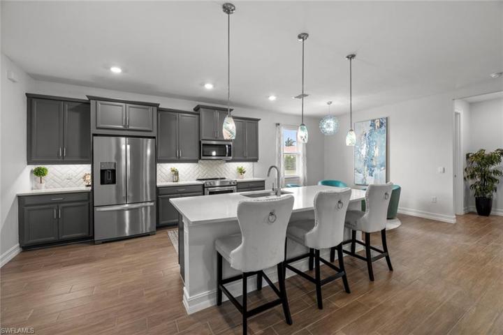 Open kitchen with WOOD-LOOK TILE FLOOR, WALK-IN PANTRY, upgraded cabinetry with crown molding, QUARTZ COUNTER, stainless steel appliances, tile backsplash, UNDER CABINET LIGHTING, and island with breakfast bar, one-bowl under mount sink, and garbage disposal. New island pendants and breakfast area chandelier (November 2022)