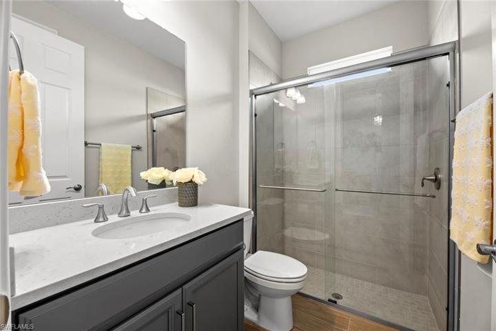 Full bath between bedrooms 3 and 4 with WOOD-LOOK TILE FLOOR, window, QUARTZ COUNTER, and tile surround shower.