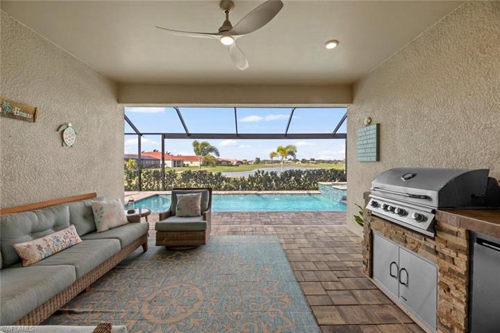 Large lanai cage with long lake and golf course views, stone new OUTDOOR KITCHEN with grill and refrigerator (June 2023), new ceiling fan/light (October 2022), and mounted flat panel TV (June 2023).