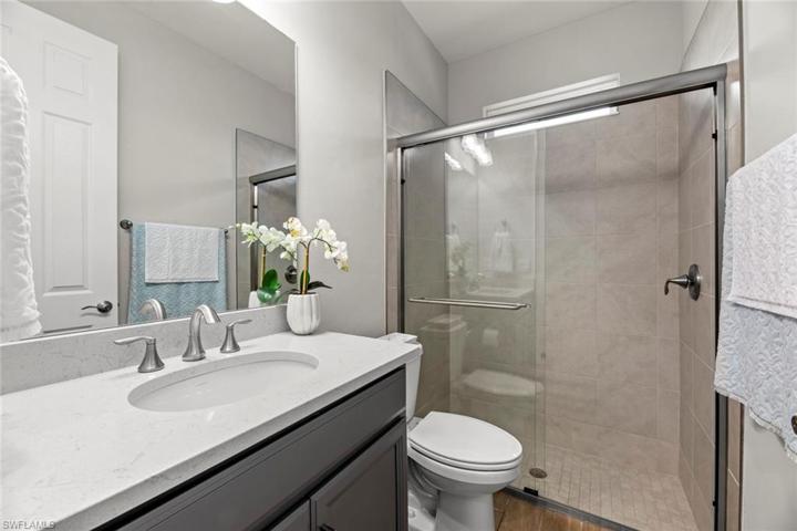 Full bath outside bedroom 2 with WOOD-LOOK TILE FLOOR, window, QUARTZ COUNTER, and tile surround shower.