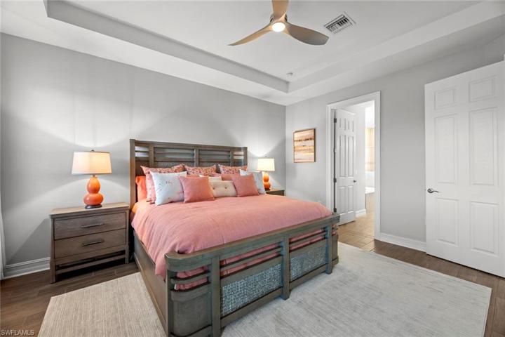 Primary suite with new WOOD-LOOK TILE FLOOR (October 2022), tray ceiling, ceiling fan/light (October 2022), window blinds, and water/golf course view.