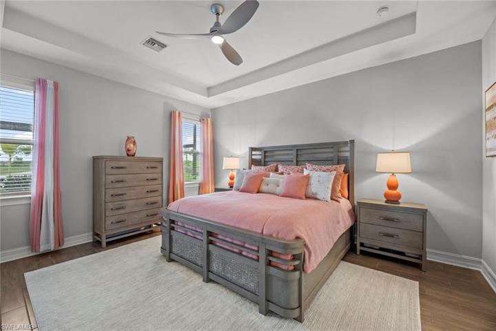 Primary suite with new WOOD-LOOK TILE FLOOR (October 2022), tray ceiling, ceiling fan/light (October 2022), window blinds, and water/golf course view.