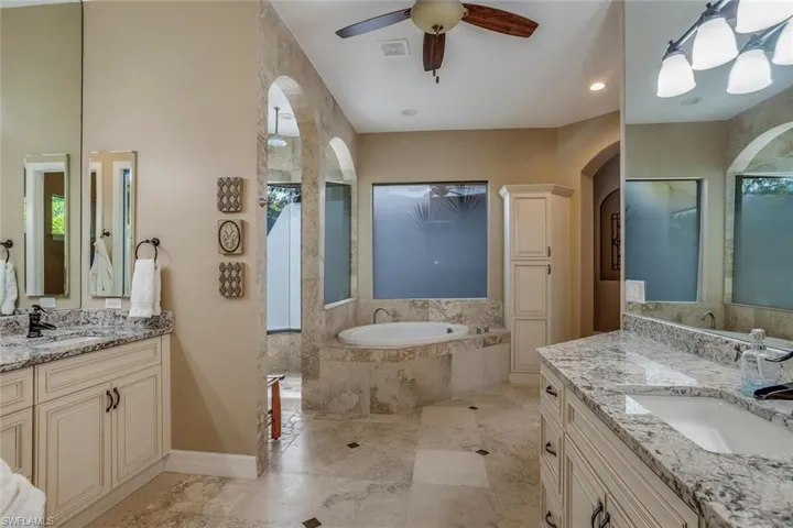 Bathroom with double station vanity, a relaxing tiled tub, extra large walk-in shower, ceiling fan, view of private garden area with a healthy amount of sunlight