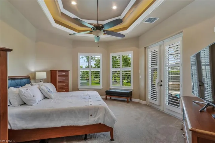 Bedroom featuring access to screened lanai, ceiling fan, crown molding, a double tray ceiling, and light carpet