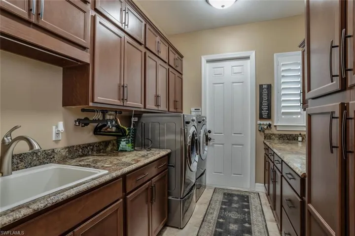 Laundry area with cabinets, front load steam washer and dryer, light tile  flooring, and sink
