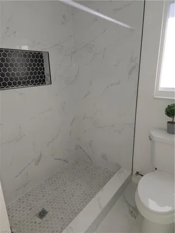 Full bath featuring a marble finish shower and marble look tile flooring