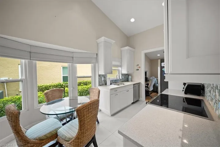 Kitchen with white cabinetry, stainless steel dishwasher, tasteful backsplash, light tile patterned floors, and high vaulted ceiling
