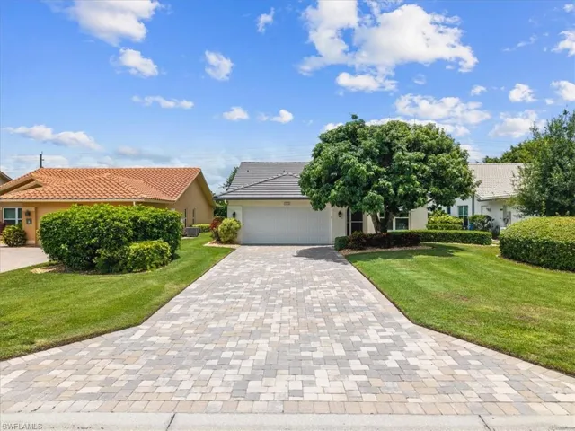 View of front of home featuring decorative driveway, an attached garage, a front lawn, and stucco siding
