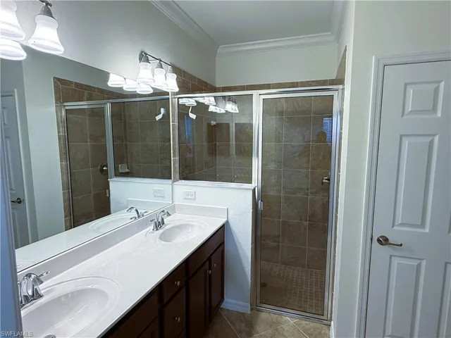 Bathroom featuring double vanity, a shower stall, ornamental molding, and light tile patterned floors