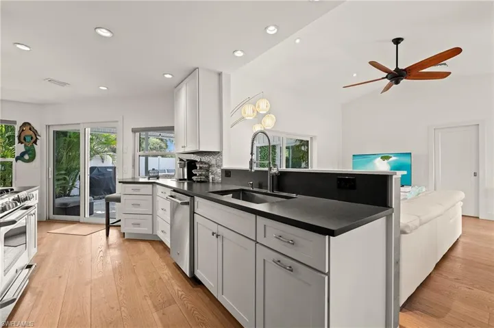 Kitchen with stainless steel appliances, a sink, white cabinetry, light wood-style floors, and dark countertops