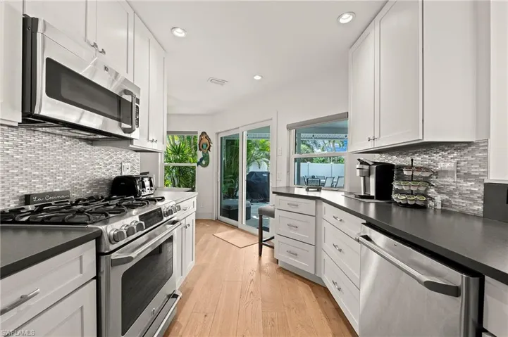 Kitchen with dark countertops, light wood-style flooring, white cabinetry, and stainless steel appliances