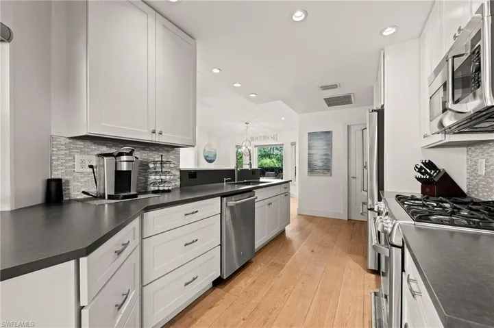 Kitchen featuring stainless steel appliances, dark countertops, white cabinetry, and a sink