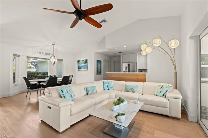 Living room with light wood finished floors, baseboards, visible vents, lofted ceiling, and ceiling fan with notable chandelier