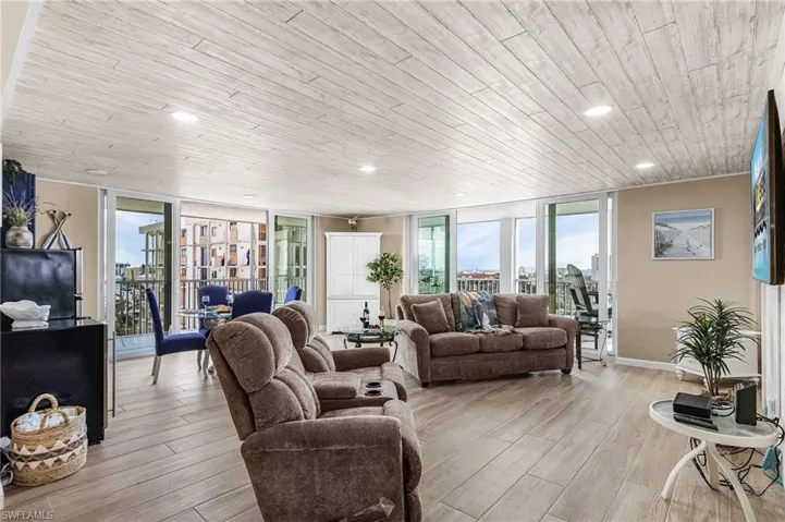 Living room featuring expansive windows, wood finish floors, wooden ceiling, and recessed lighting - Virtually Edited Image