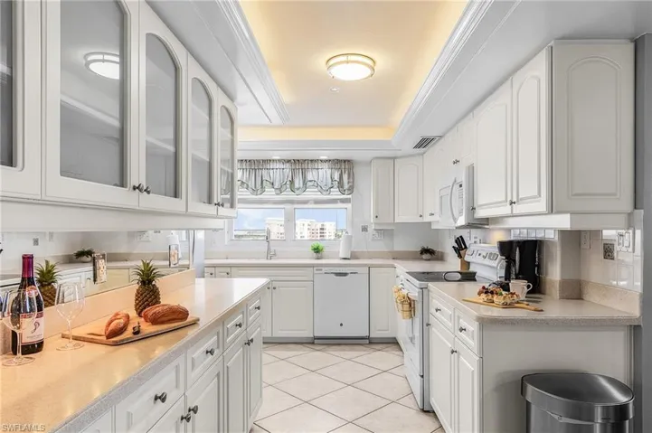 Kitchen featuring white cabinets, white appliances, light tile patterned flooring, and glass fronted cabinets - Virtually Edited Image