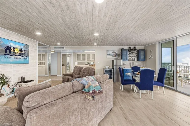 Living room with wine cooler, light wood-style floors, wooden ceiling, recessed lighting, and floor to ceiling windows - Virtually Edited Image