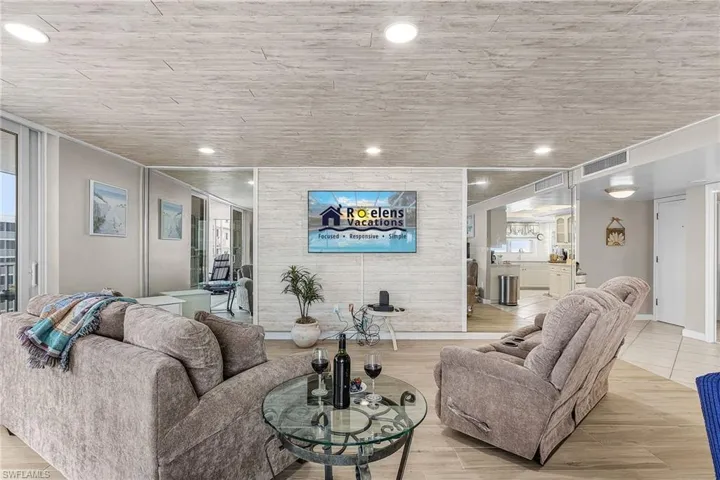 Living room featuring light wood finished floors, an accent wall, and recessed lighting - Virtually Edited Image