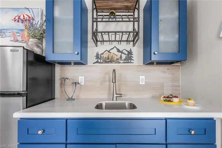 Kitchen featuring blue cabinetry, freestanding refrigerator, light countertops, and tasteful backsplash - Virtually Edited Image