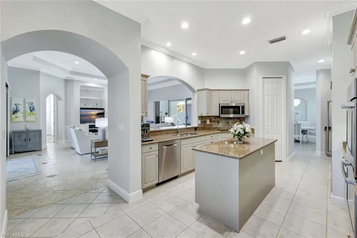 Kitchen with appliances with stainless steel finishes, light stone counters, sink, light tile patterned floors, and a center island