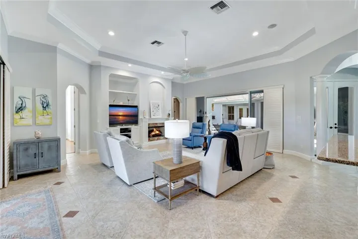 Living room with decorative columns, ornamental molding, built in shelves, a tray ceiling, and ceiling fan