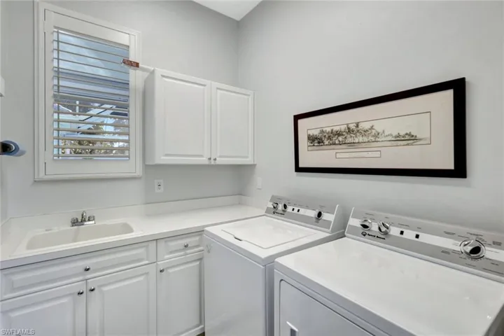 Clothes washing area with washing machine and dryer, sink, and cabinets