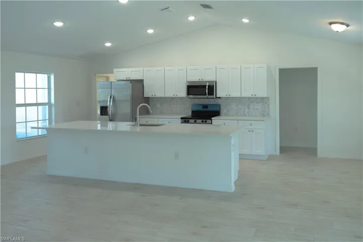 Kitchen featuring vaulted ceiling, stainless steel appliances, and white cabinets