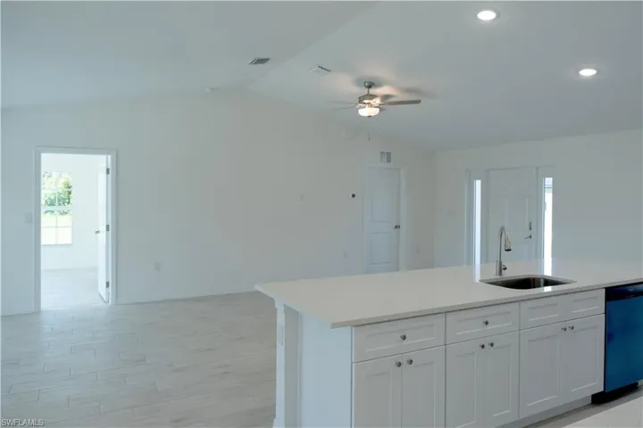 Kitchen featuring dishwashing machine, sink, white cabinets, ceiling fan, and vaulted ceiling