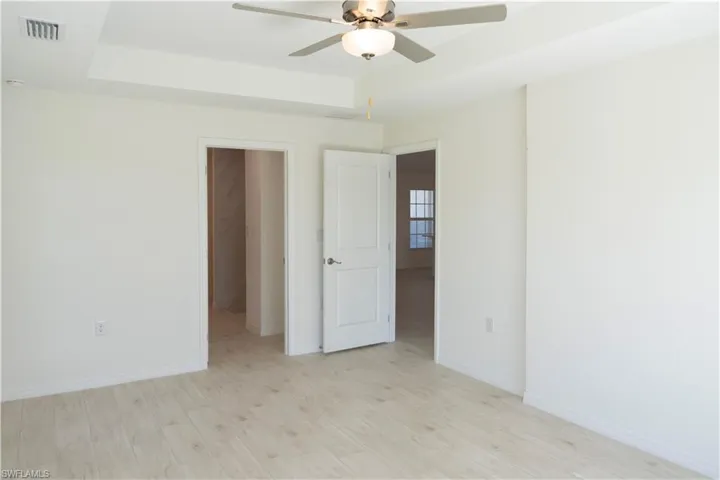 Empty room with a tray ceiling, ceiling fan, and light hardwood / wood-style floors