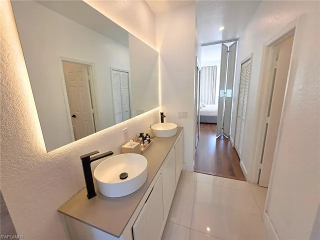 Bathroom with a textured wall, double vanity, light tile patterned floors, and a closet