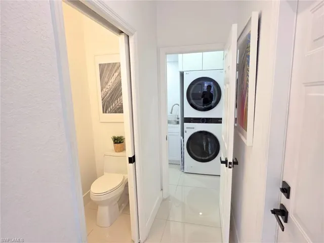 Bathroom featuring tile patterned floors, a textured wall, and stacked washing machine and dryer