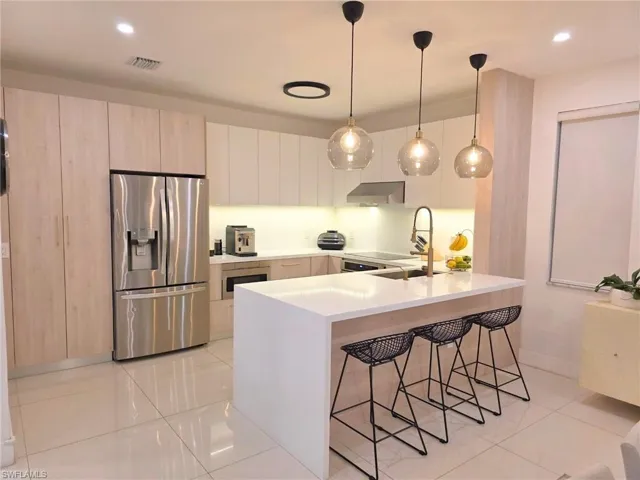 Kitchen featuring a peninsula, a kitchen breakfast bar, stainless steel appliances, hanging light fixtures, and light tile patterned floors