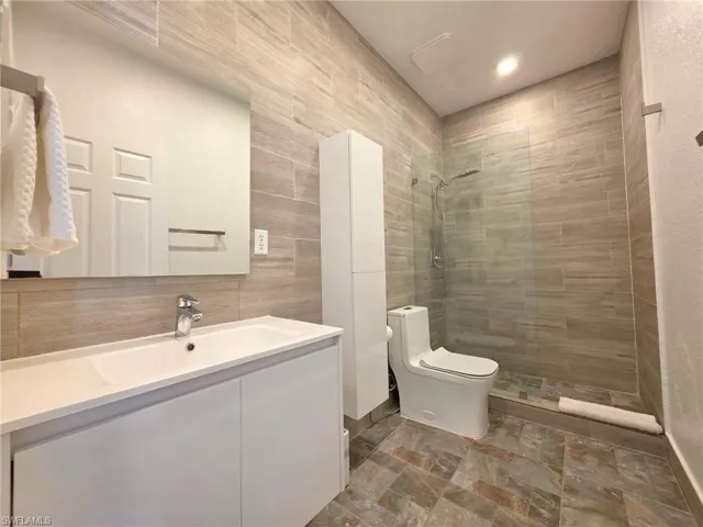 Full bathroom with walk in shower, vanity, tile walls, dark stone finish flooring, and recessed lighting