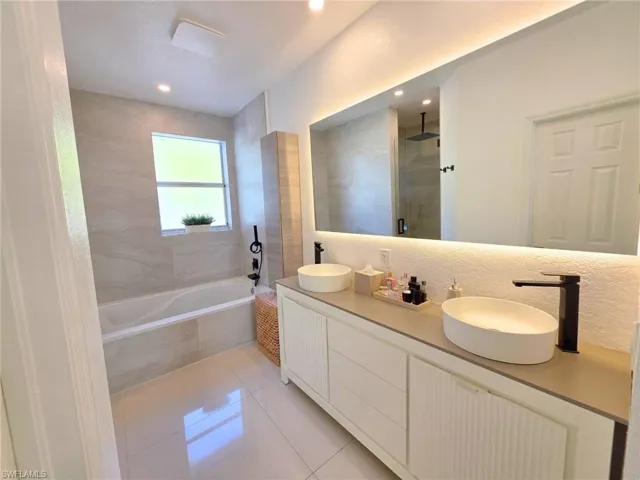 Full bath featuring light tile patterned flooring, double vanity, a tile shower, and tiled bath