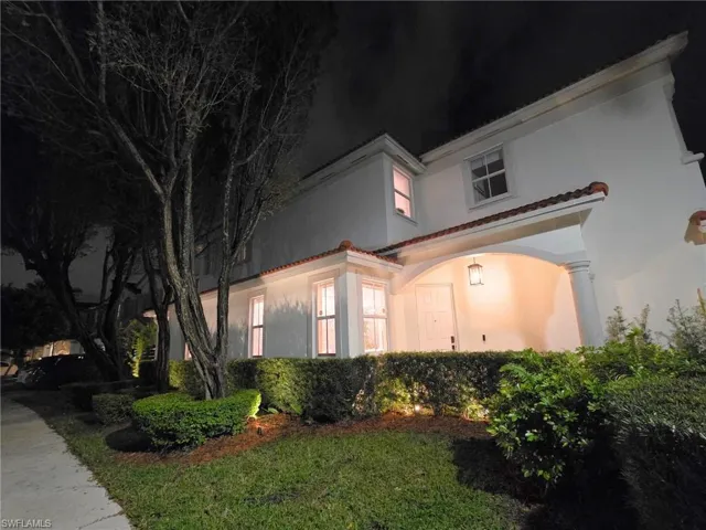 Property exterior at night with stucco siding, a tiled roof, and a lawn