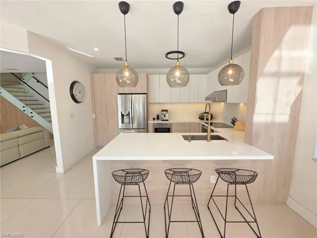 Kitchen with a breakfast bar area, modern cabinets, stainless steel refrigerator with ice dispenser, light stone countertops, and hanging light fixtures