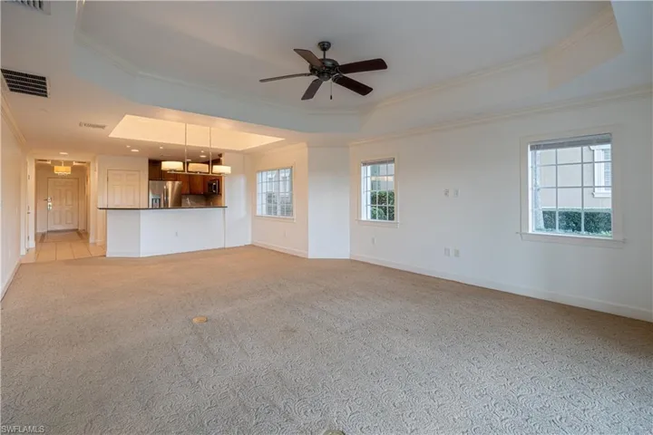 Unfurnished living room featuring crown molding, ceiling fan, light colored carpet, and a raised ceiling