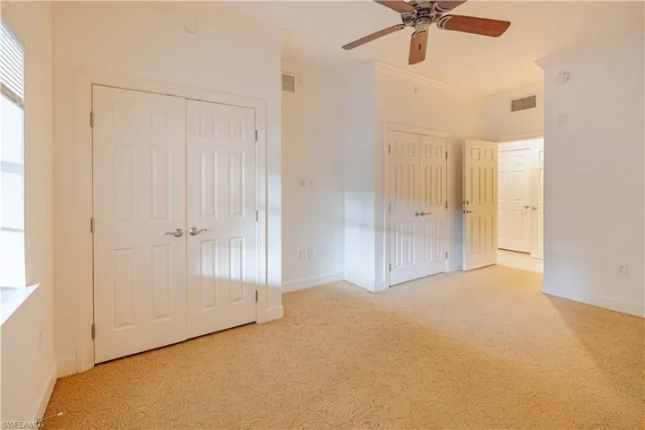 Unfurnished bedroom with multiple closets, ornamental molding, ceiling fan, and light colored carpet