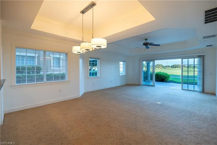 Unfurnished living room with ceiling fan with notable chandelier, a tray ceiling, and carpet flooring