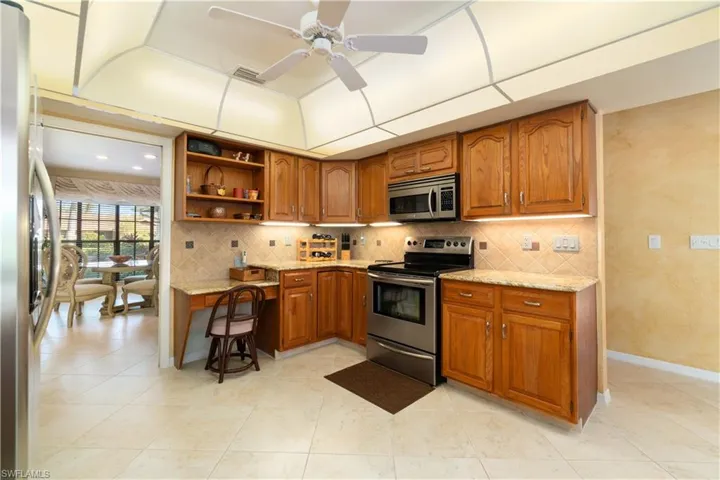 Kitchen with decorative backsplash, appliances with stainless steel finishes, light stone counters, and ceiling fan