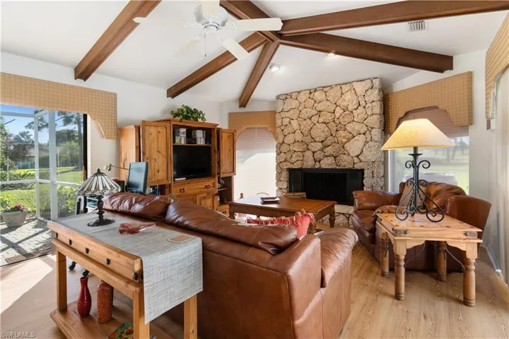 Living room with vaulted ceiling with beams, ceiling fan, a stone fireplace, and light hardwood / wood-style flooring