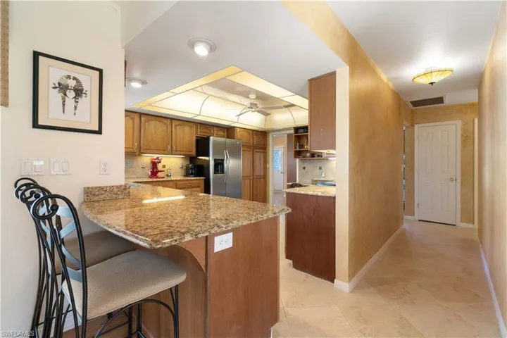 Kitchen featuring kitchen peninsula, stainless steel fridge, a kitchen breakfast bar, light stone counters, and ceiling fan