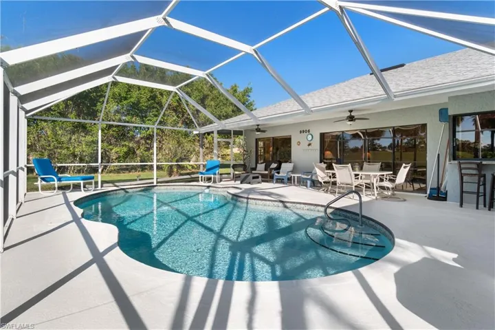 View of pool with glass enclosure, ceiling fan, and a patio area