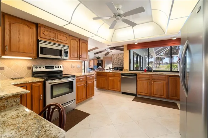 Kitchen featuring light stone countertops, appliances with stainless steel finishes, vaulted ceiling, and ceiling fan