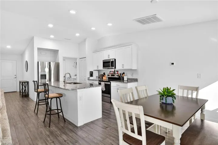 Kitchen featuring dark stone counters, stainless steel appliances, a center island with sink, white cabinetry, and a breakfast bar area