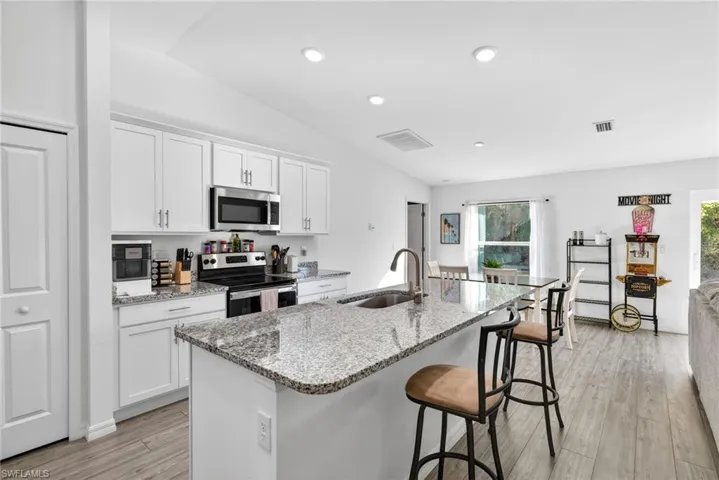Kitchen featuring light stone countertops, appliances with stainless steel finishes, a center island with sink, white cabinets, and a kitchen breakfast bar