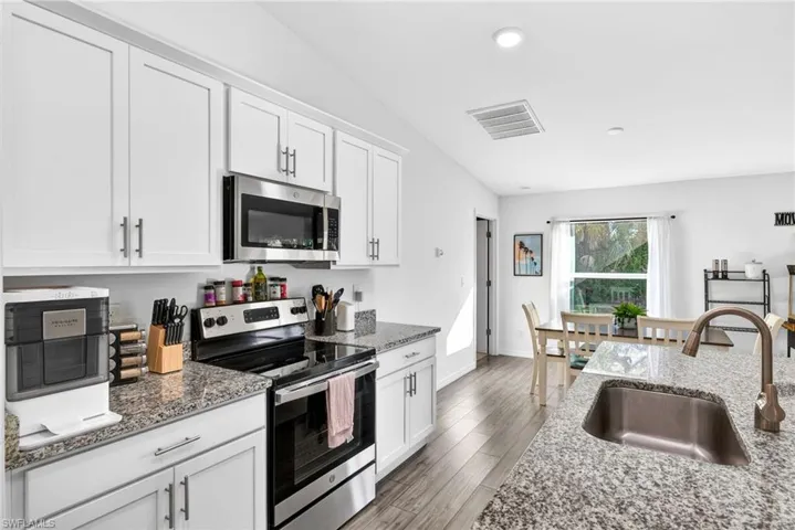 Kitchen with stainless steel appliances, white cabinets, dark stone counters, light wood-style flooring, and recessed lighting