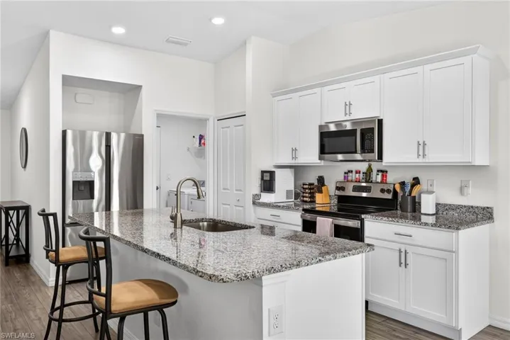 Kitchen with light stone counters, appliances with stainless steel finishes, light wood-type flooring, white cabinets, and a center island with sink