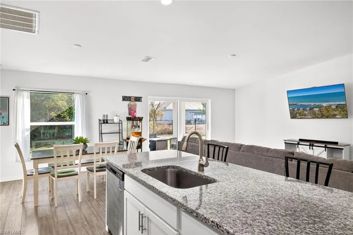 Kitchen featuring white cabinetry, light stone countertops, open floor plan, light wood-type flooring, and dishwasher