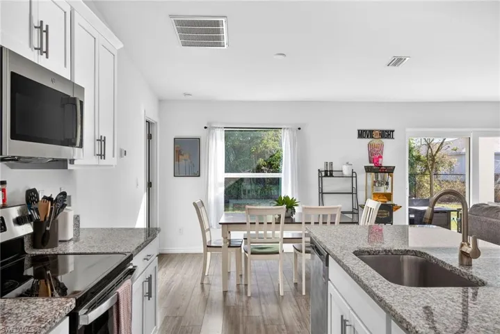 Kitchen featuring appliances with stainless steel finishes, white cabinetry, light stone countertops, and dark wood-style flooring