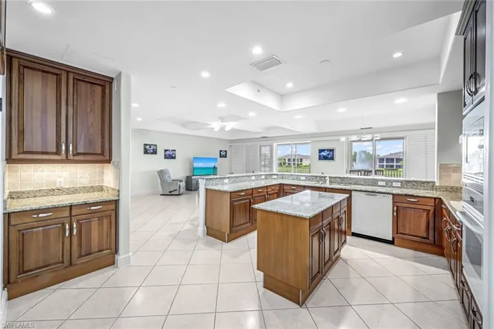 Kitchen featuring tasteful backsplash, light stone counters, a peninsula, a tray ceiling, and white appliances